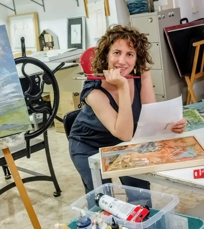 Diana Cordero en su estudio de arte, sosteniendo pinceles y observando un boceto.